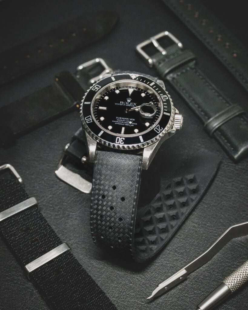 Rolex Submariner montée sur un bracelet en caoutchouc tropic avec en arrière-plan un bracelet nato et un bracelet en cuir noir